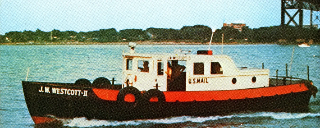 Small boat on river under a bridge, white and red with black tires as bumpers, trees in the background.