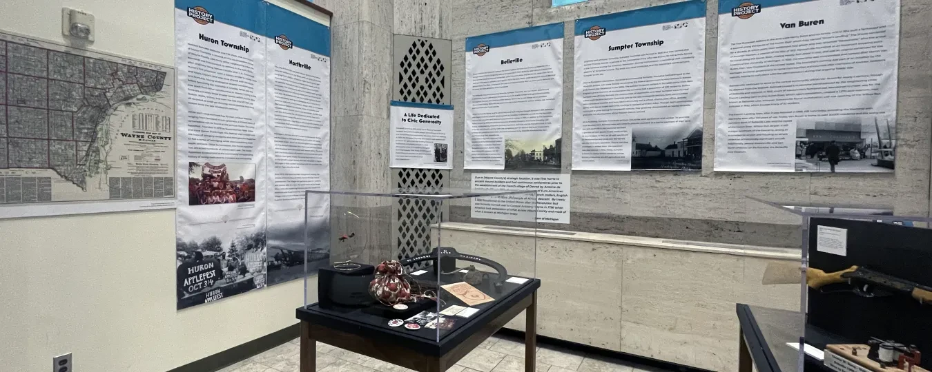 Museum exhibit room with informational panels on walls, display tables with artifacts, and blue-tinted windows.