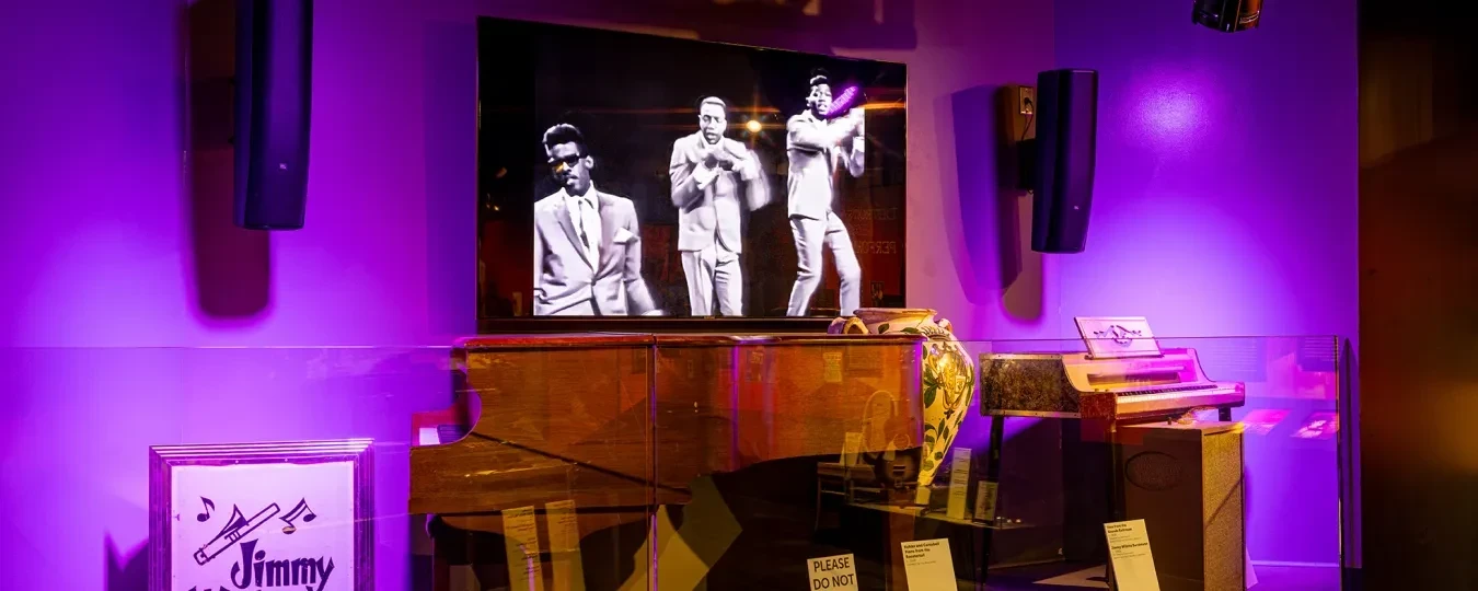 Stage with purple lighting, vintage piano, and a screen showing black and white performers.