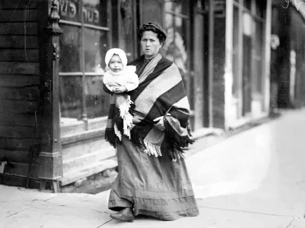 Woman and baby walking in front of a Kosher butcher shop.