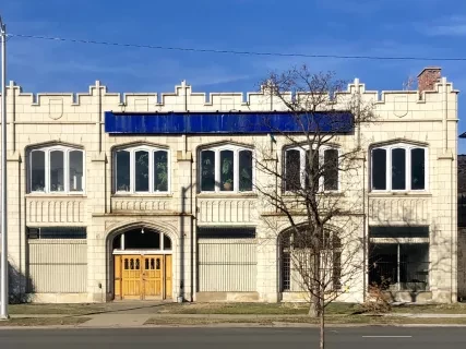 Historic building with white facade, multiple windows, and a large blue sign, set against a clear blue sky.
