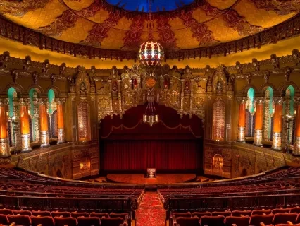 Ornate theater with red curtains, arched windows, and intricate ceiling, viewed from the balcony.