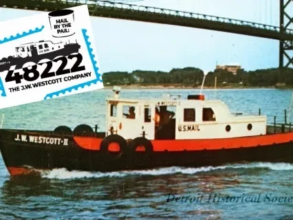 White and red boat J.W. Westcott II on a river, with a bridge and distant buildings in the background.