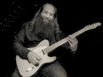 Bearded man playing electric guitar, smiling.