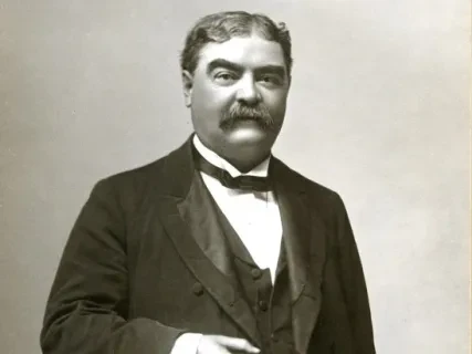 Man in formal Victorian attire with a mustache, holding a pocket watch. Black and white photograph.