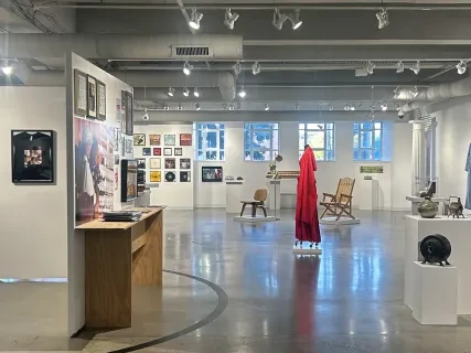 Spacious art gallery with various framed artworks on white walls, sculptures, and a bright red dress in the center.