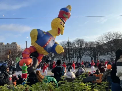 Parade scene with a Big Bird balloon float in the sky; crowd and trees in the background.