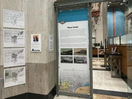 Display panel in a hallway with maps and text about Wayne County. Contains historical photos and maps on the left wall.