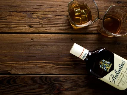 Bottle of whiskey lies flat on a wooden table beside two glasses filled with whiskey.