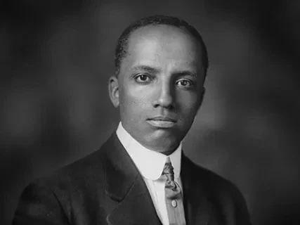 Black and white portrait of Carter Woodson in a suit and tie, with a serious expression.