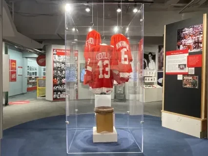 Red sports jerseys displayed in a glass case in a brightly lit museum exhibit.