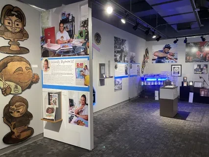 Exhibit room with cartoon murals, informational panels, and art displays under spotlights in a modern setting.