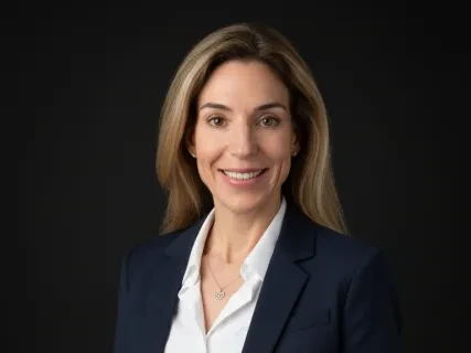Smiling woman in a navy suit with a white shirt against a black background.