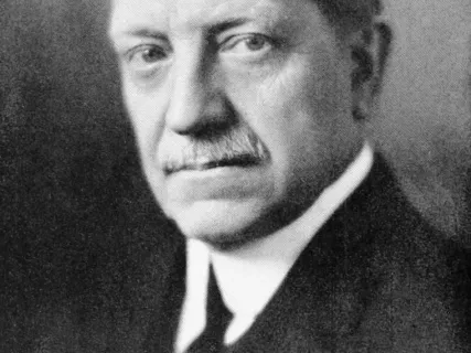 Black and white portrait of a man in a suit with a stern expression.