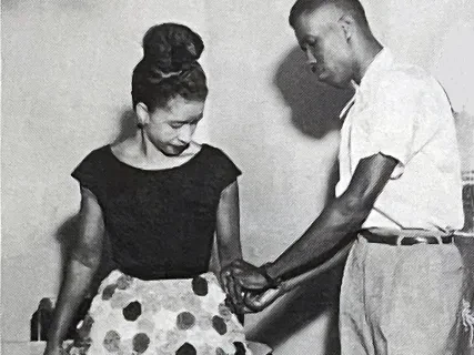A man offers assistance to a woman wearing a polka dot skirt.