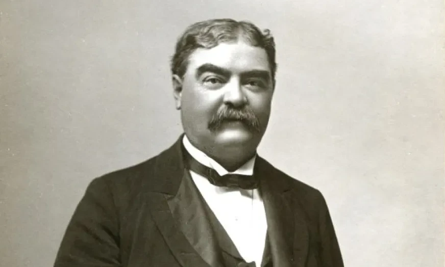 Man in formal Victorian attire with a mustache, holding a pocket watch. Black and white photograph.