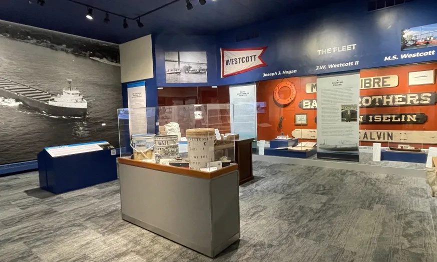 Museum exhibit room with nautical-themed displays, model ships, and historical photos on the blue and red walls.