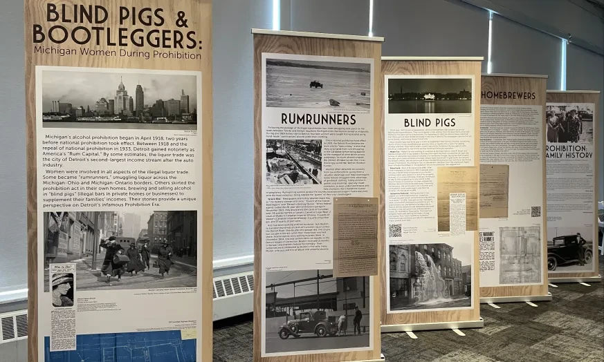 Exhibition banners display historical content on blind pigs and bootleggers in a room with carpeted floor and natural lighting.