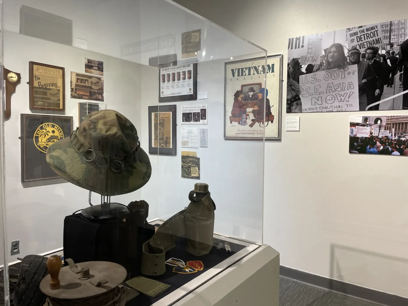 Museum exhibit with Vietnam War memorabilia, including a helmet and posters, displayed in a glass case.