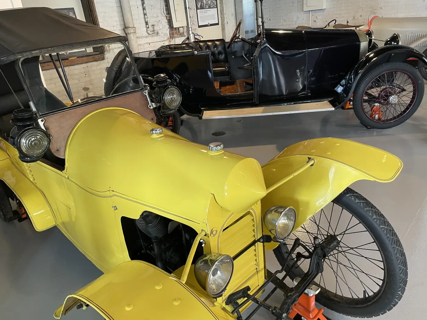 Yellow vintage car in a showroom, displayed next to a black vintage car.