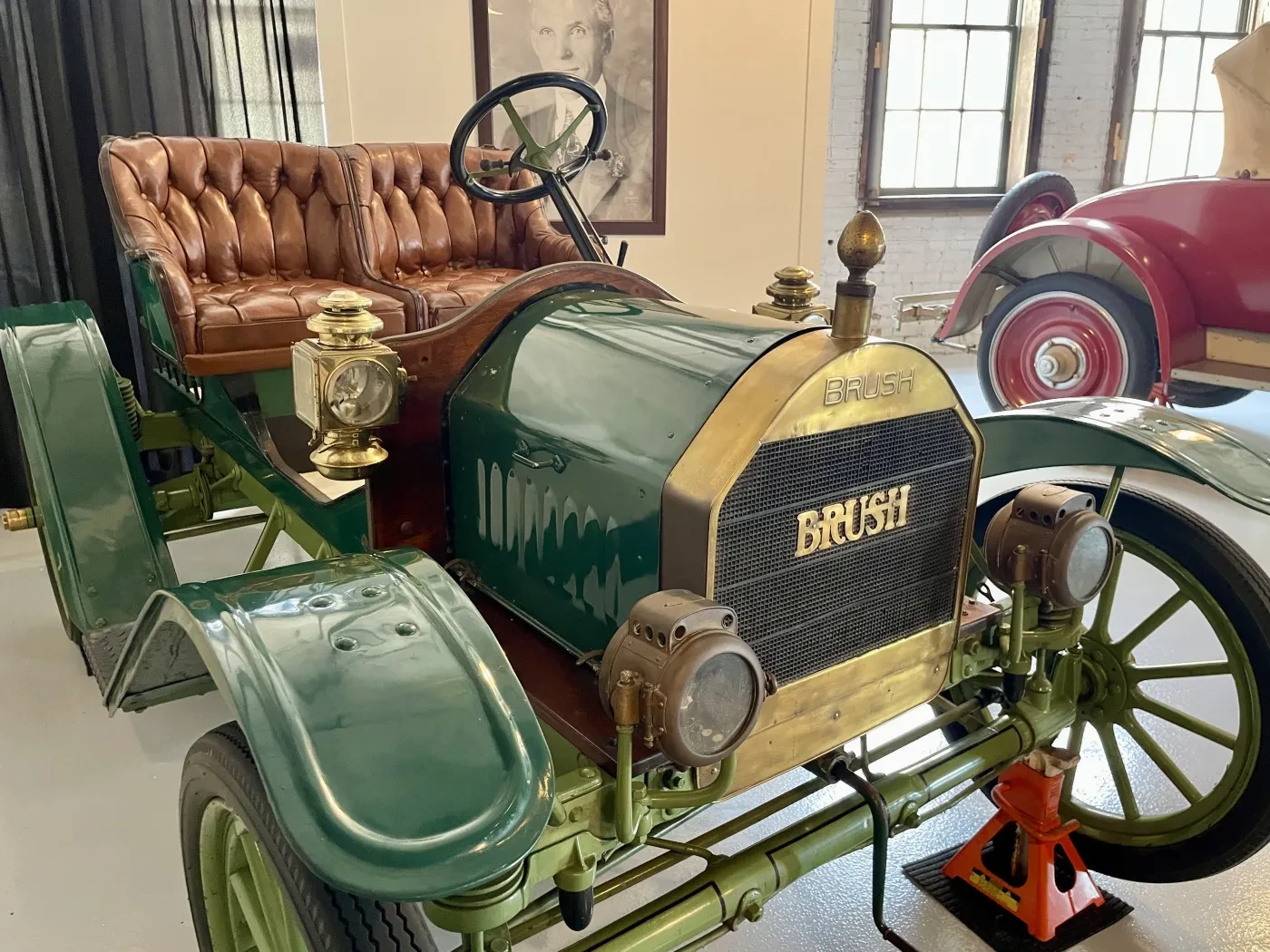 Antique green car with brass details and a tufted leather seat in a museum setting.