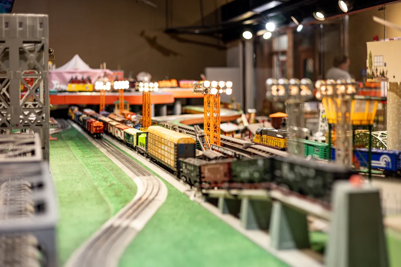 A model train display with various tracks, colorful trains, and lit structures in a detailed miniature setting.