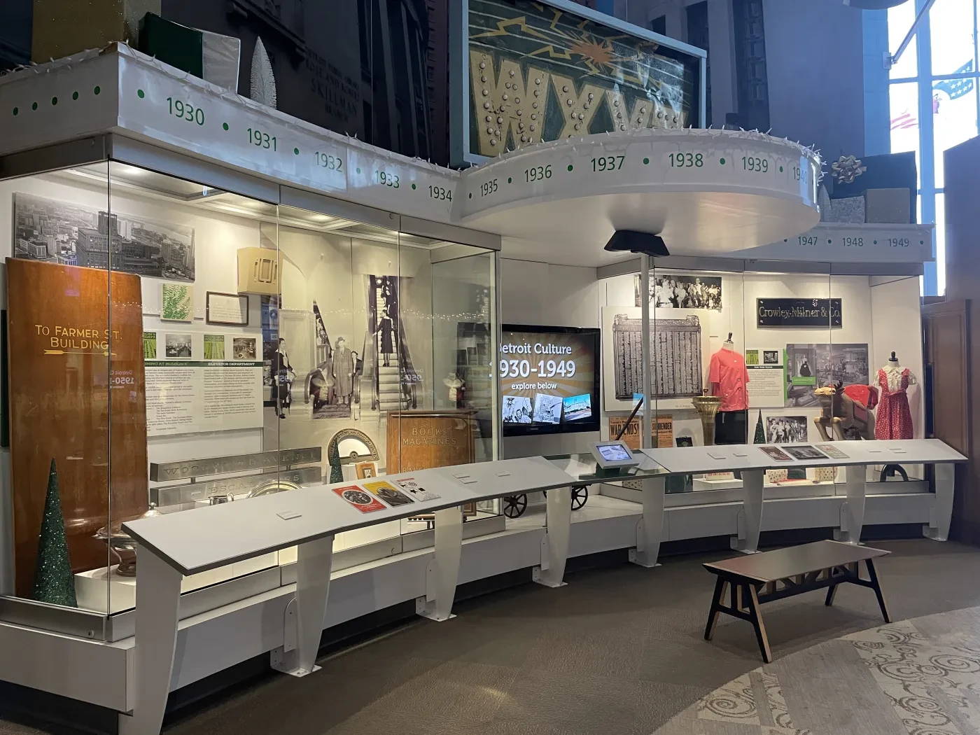 Museum exhibit with photos, artifacts, and a bench. Display cases have historic items and a model bridge.