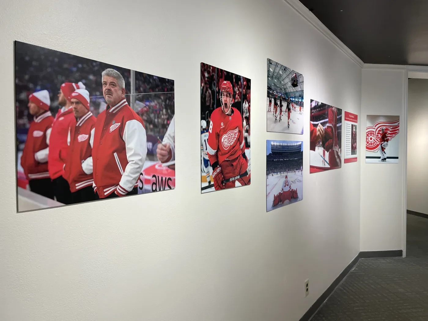 Hallway wall with framed sports photographs, mainly featuring people in red jackets and team memorabilia.