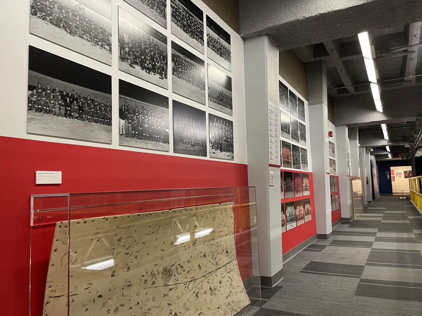Museum hallway with black-and-white photos on red walls, gray carpet, and display cases.