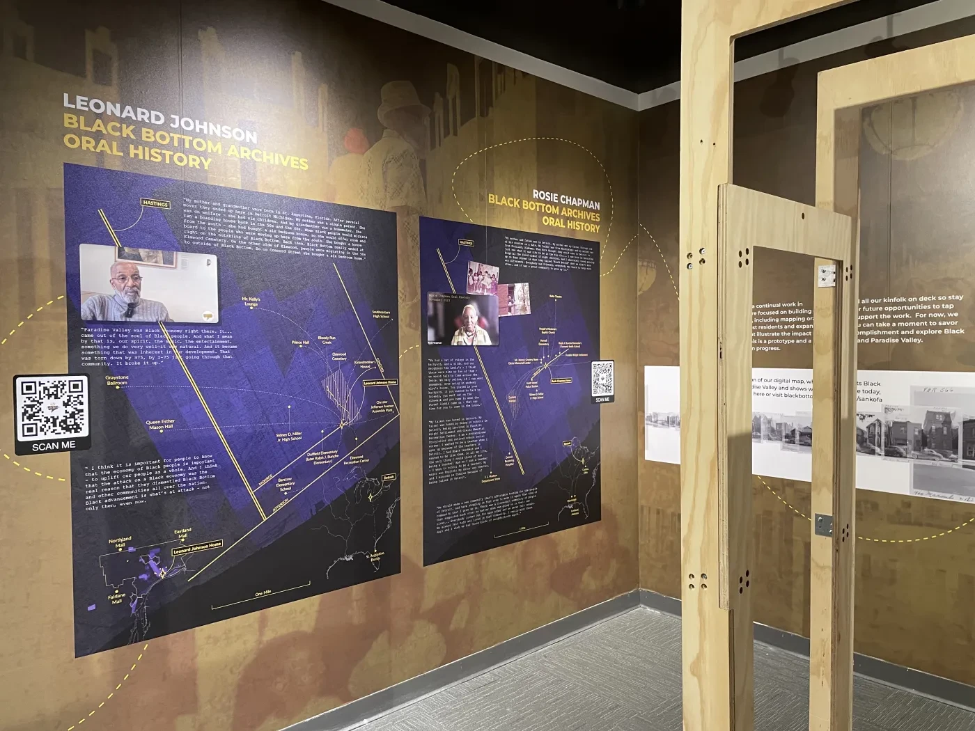 Exhibit with wooden frames, blue informational panels, and video displays on a brown wall.