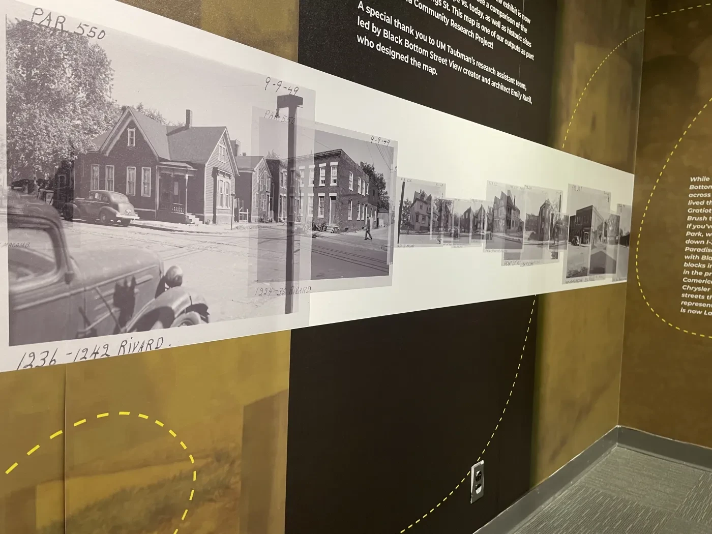 Black and white historical photographs displayed on a museum wall, depicting a timeline of buildings.