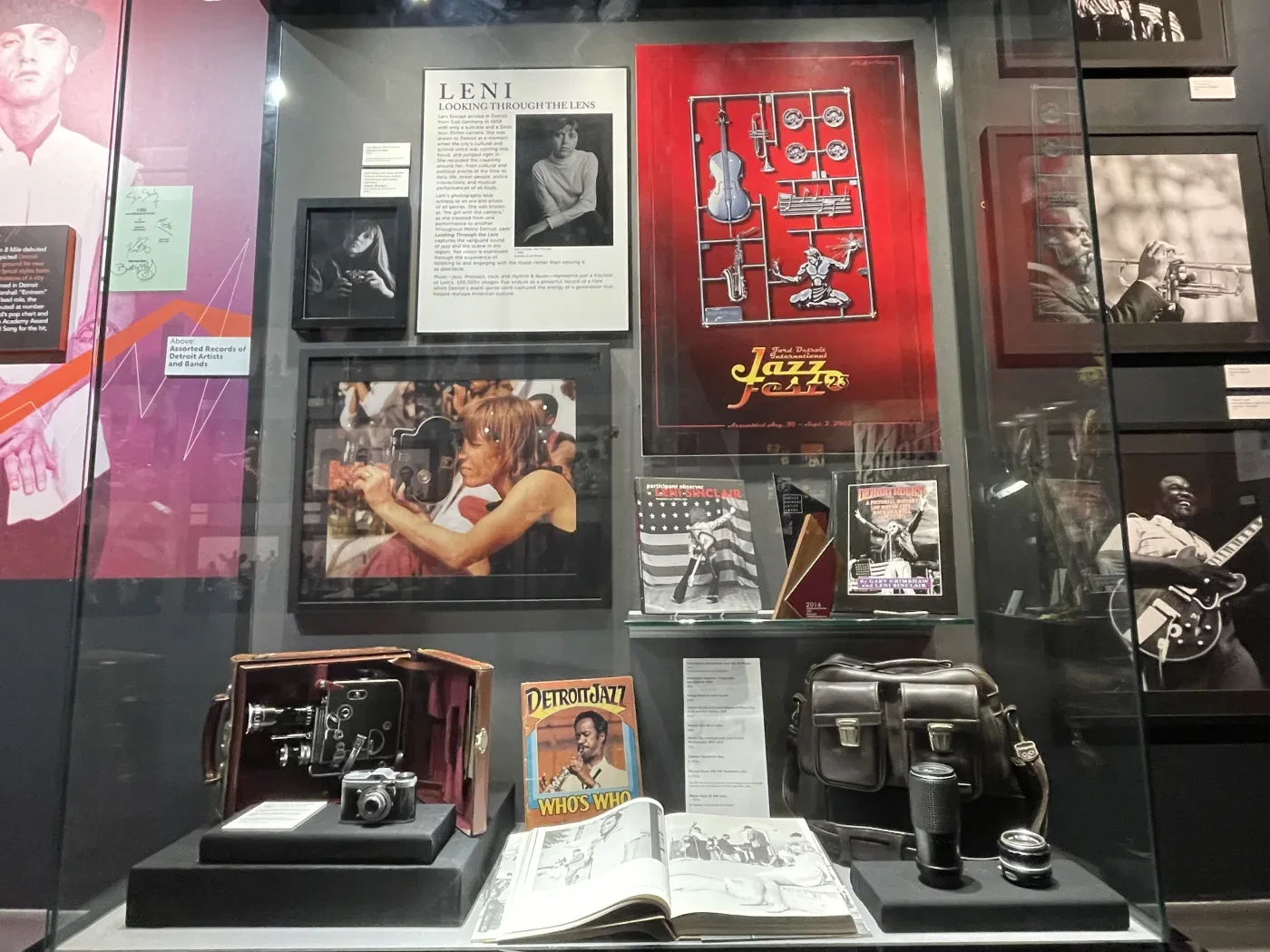 Museum exhibit with vintage cameras, photographs, a red guitar-themed sign, and black-and-white portraits.