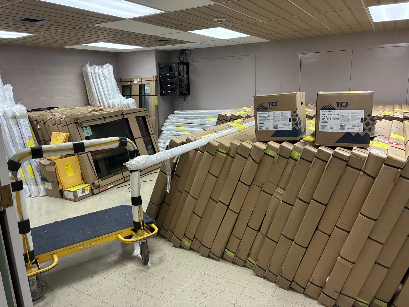 Boxes piled against a wall in a storage room with yellow carts.