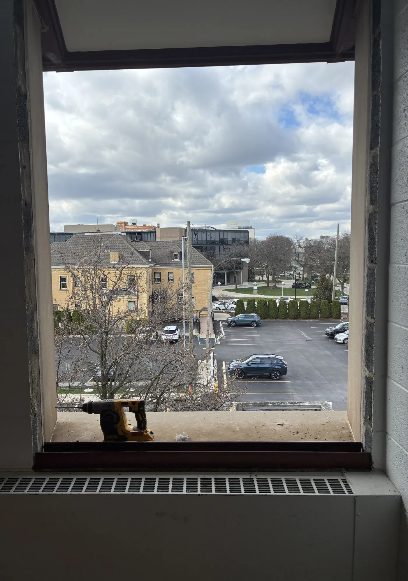 View through a window of a parking lot and buildings under a cloudy sky.