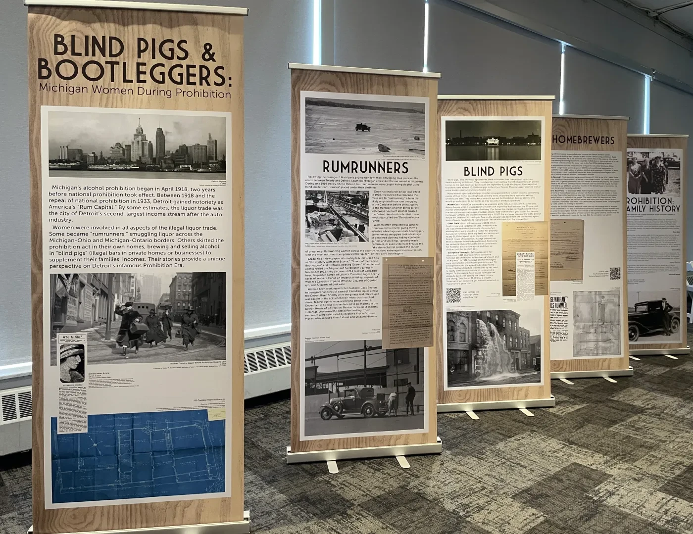 Exhibition banners display historical content on blind pigs and bootleggers in a room with carpeted floor and natural lighting.