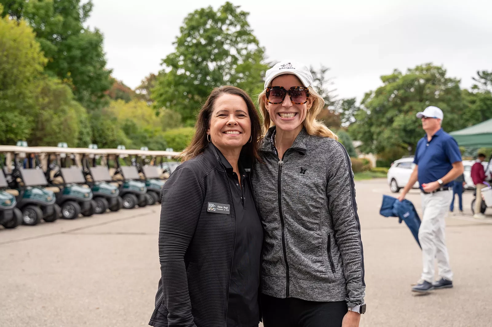 Two women smiling, standing outside near parked golf carts.
