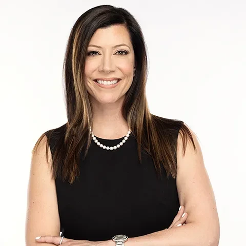 Smiling woman in black dress with crossed arms against a white background.