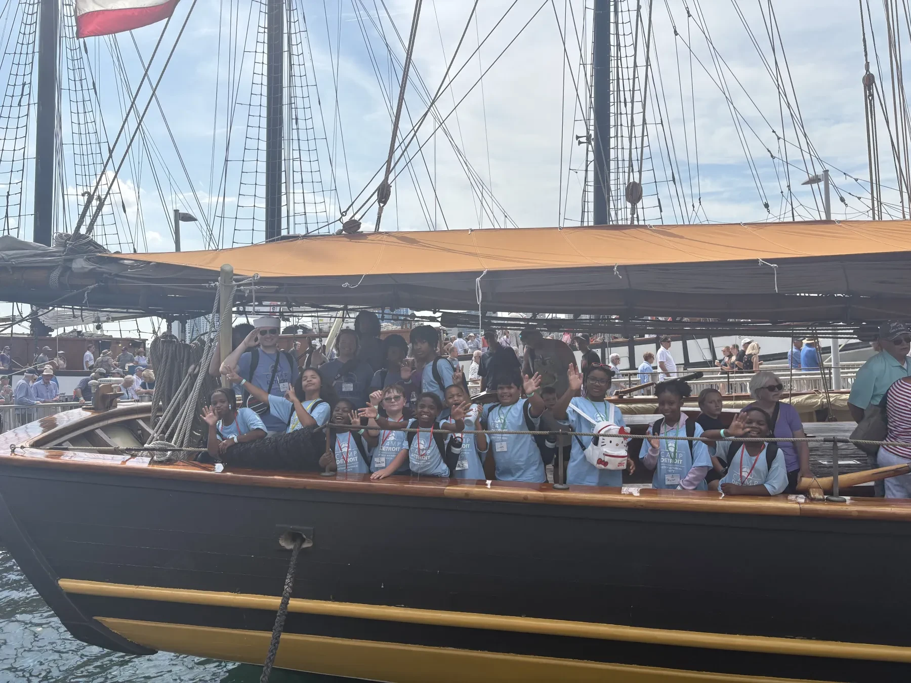Group of people wearing life vests on a large sailboat docked at a harbor.