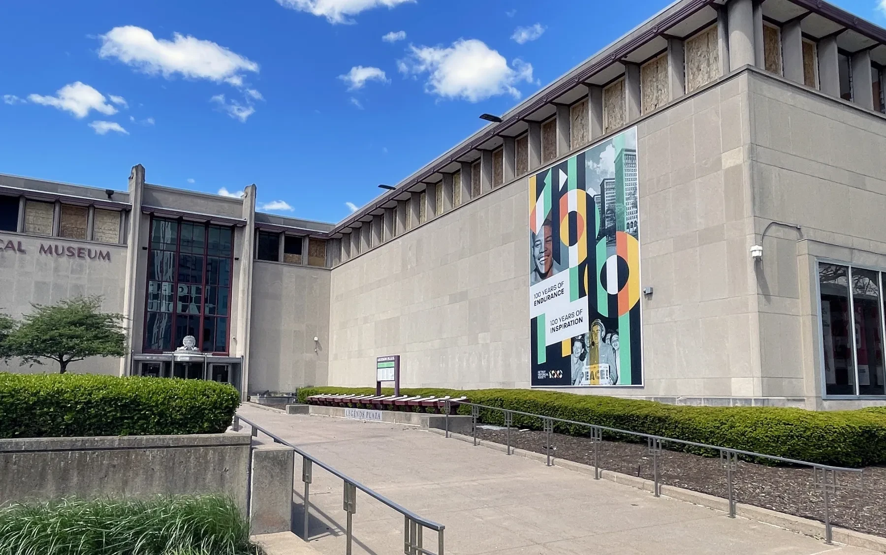Large museum building with modern facade, colorful banner, and pathway, under a blue sky with clouds.